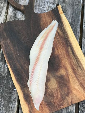 A filet of locally-caught fish, atop a wooden cutting board.